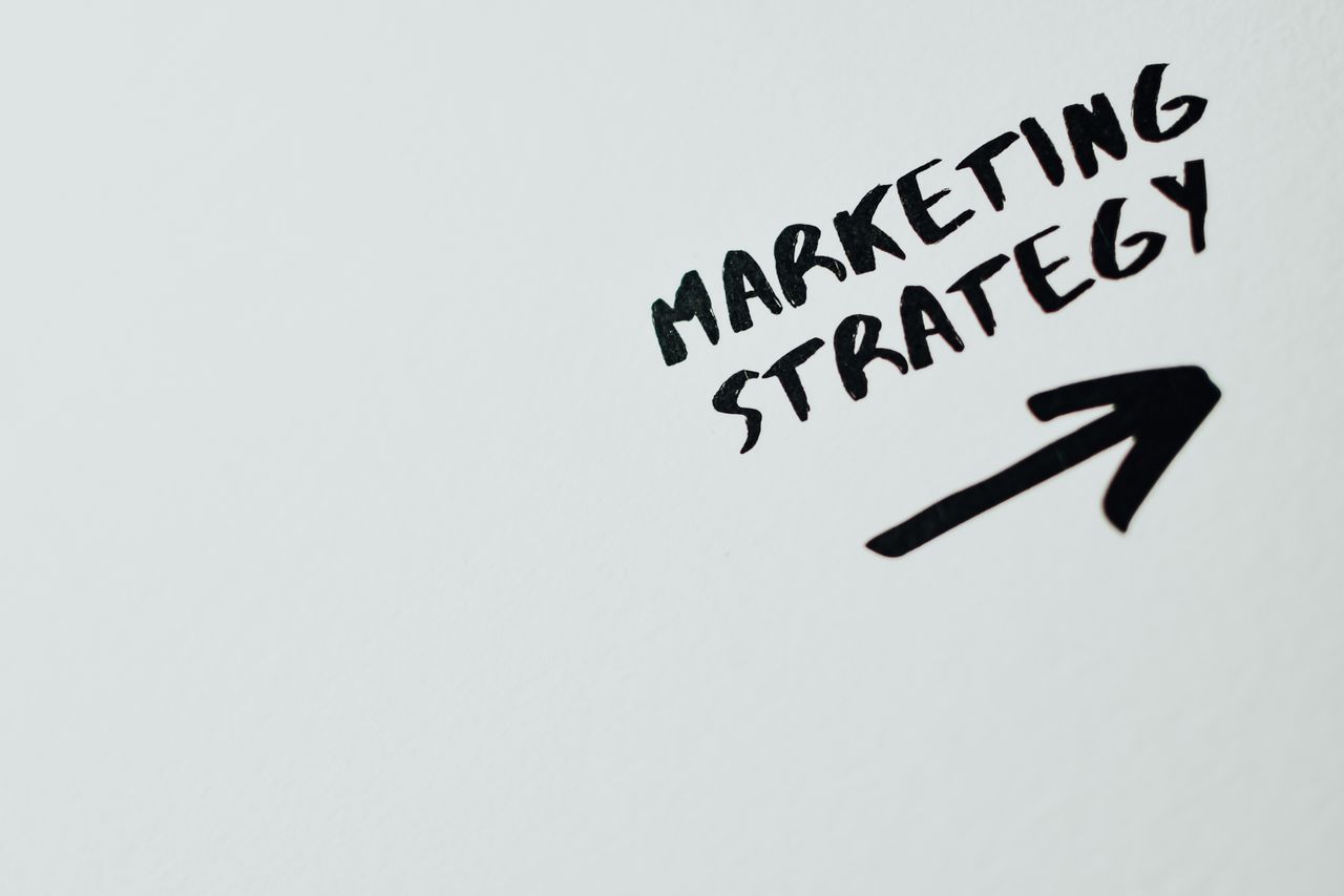 team-01 Close-up of handwritten Marketing Strategy text with an arrow on white background.